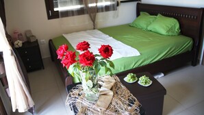 A neatly arranged bedroom with a green bedspread, a white towel, and a vase of red roses on a wicker table. - AM Beach House near Sea (Nea Propontida)