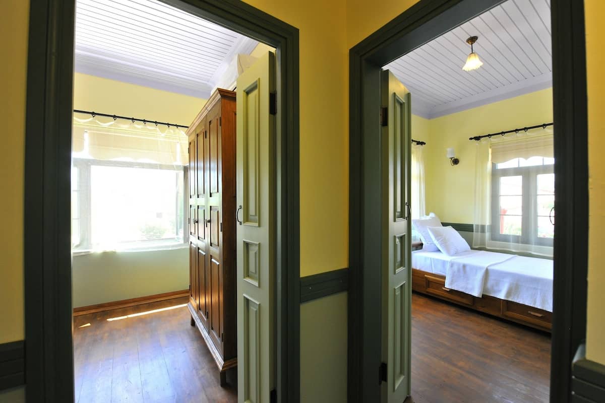 A hallway leading to a bedroom with a bed, a window with curtains, and wooden flooring.
