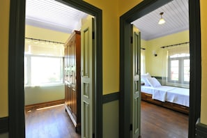 A hallway leading to a bedroom with a bed, a window with curtains, and wooden flooring. - Petrino Gokceada Hotel & Kitchen (Gökçeada)