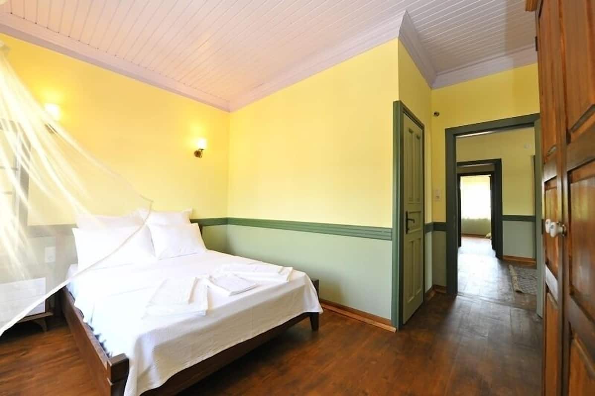 A bedroom with a bed, wooden floor, and a door leading to another room.