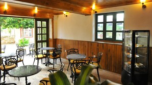 Um espaço de refeições interno com paredes de madeira, uma vitrine de vidro com sobremesas e várias mesas e cadeiras.
