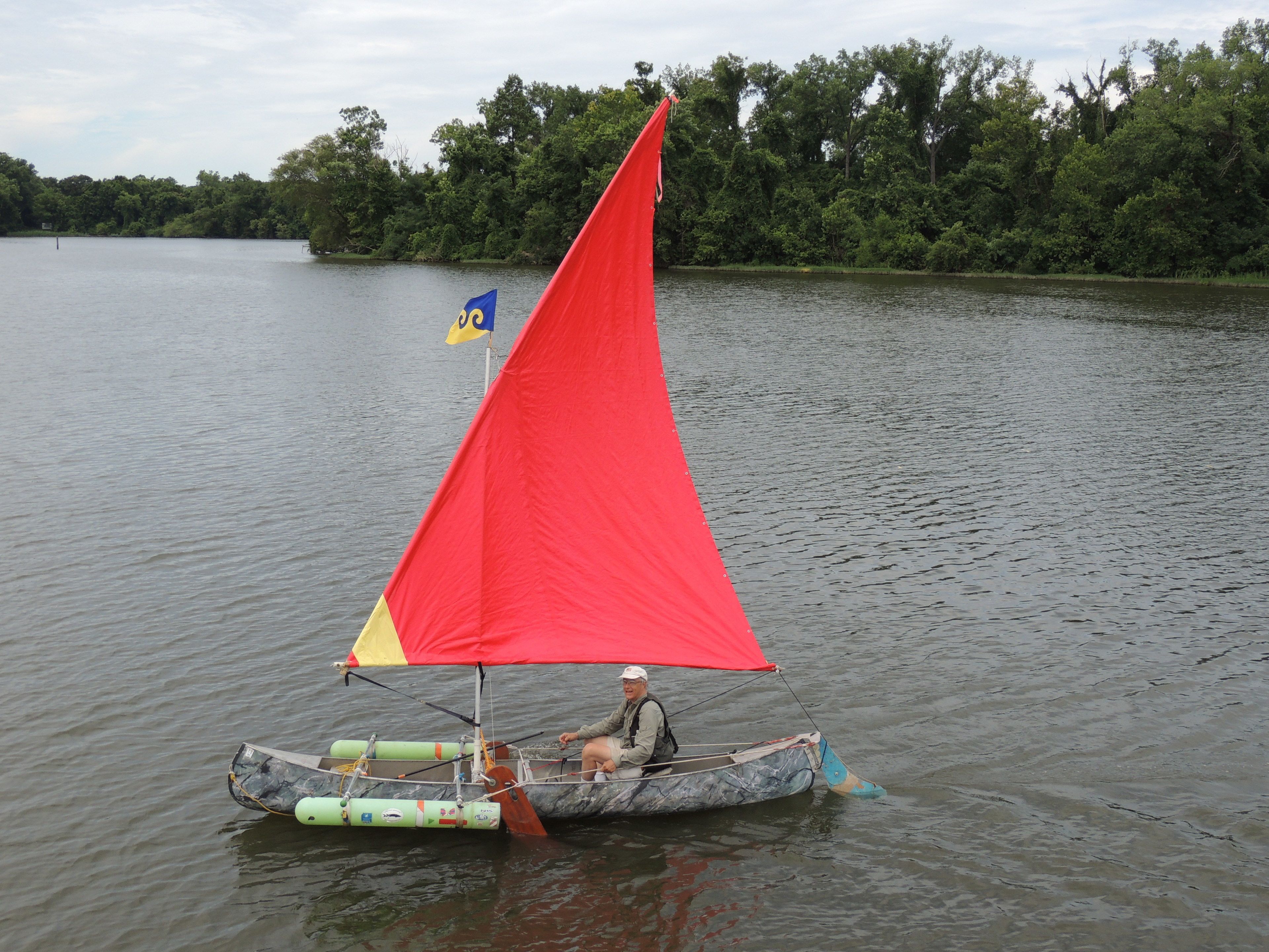 A person in a small boat with a red sail on a calm lake.