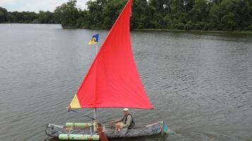 A person in a small boat with a red sail on a calm lake.