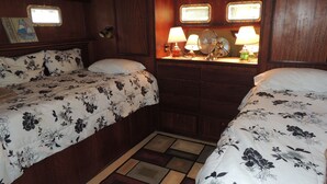 Une chambre avec deux lits, un lambris en bois, une petite fenêtre et une table de chevet avec des lampes.