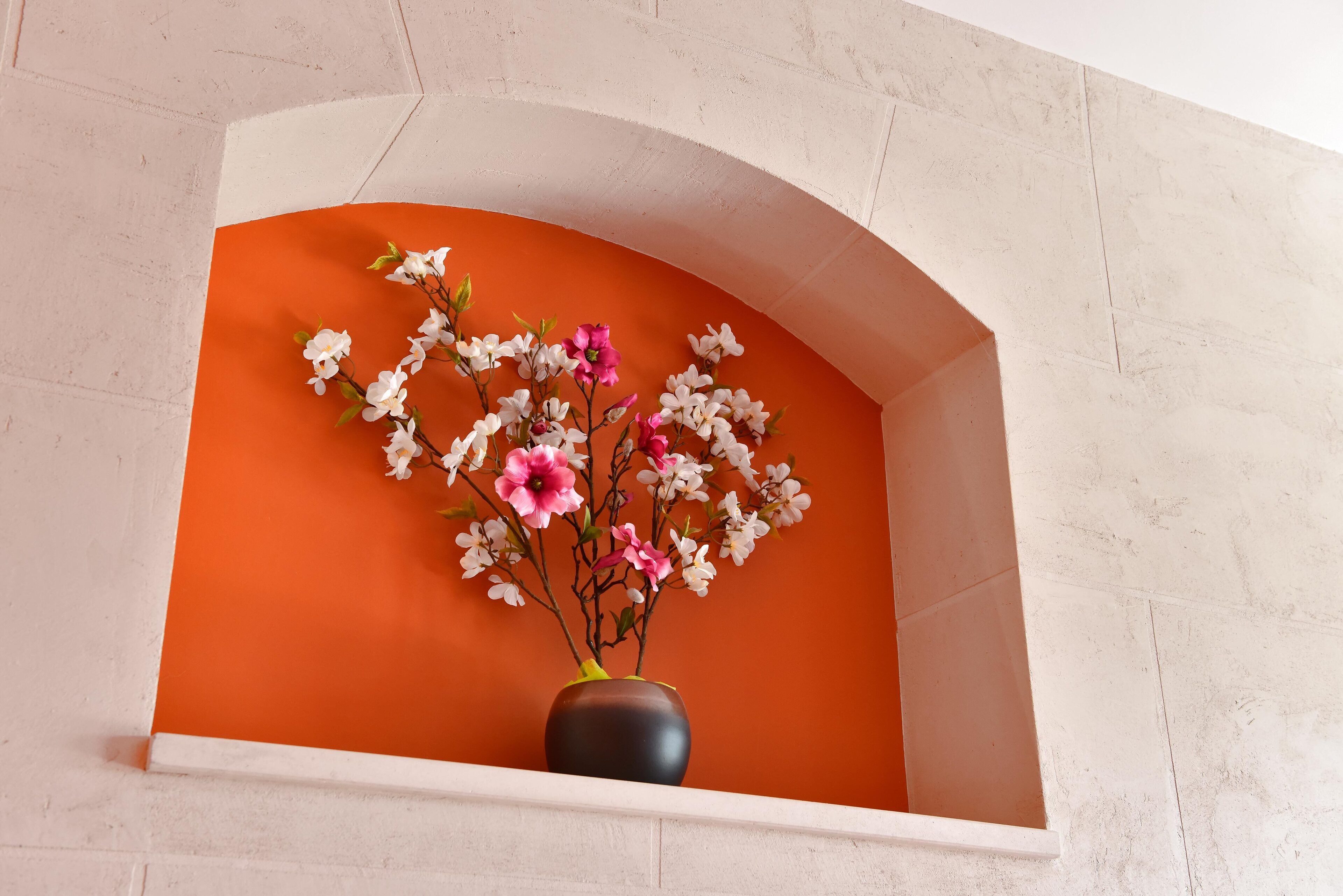 Een vaas met bloemen in een witte nis tegen een oranje muur.