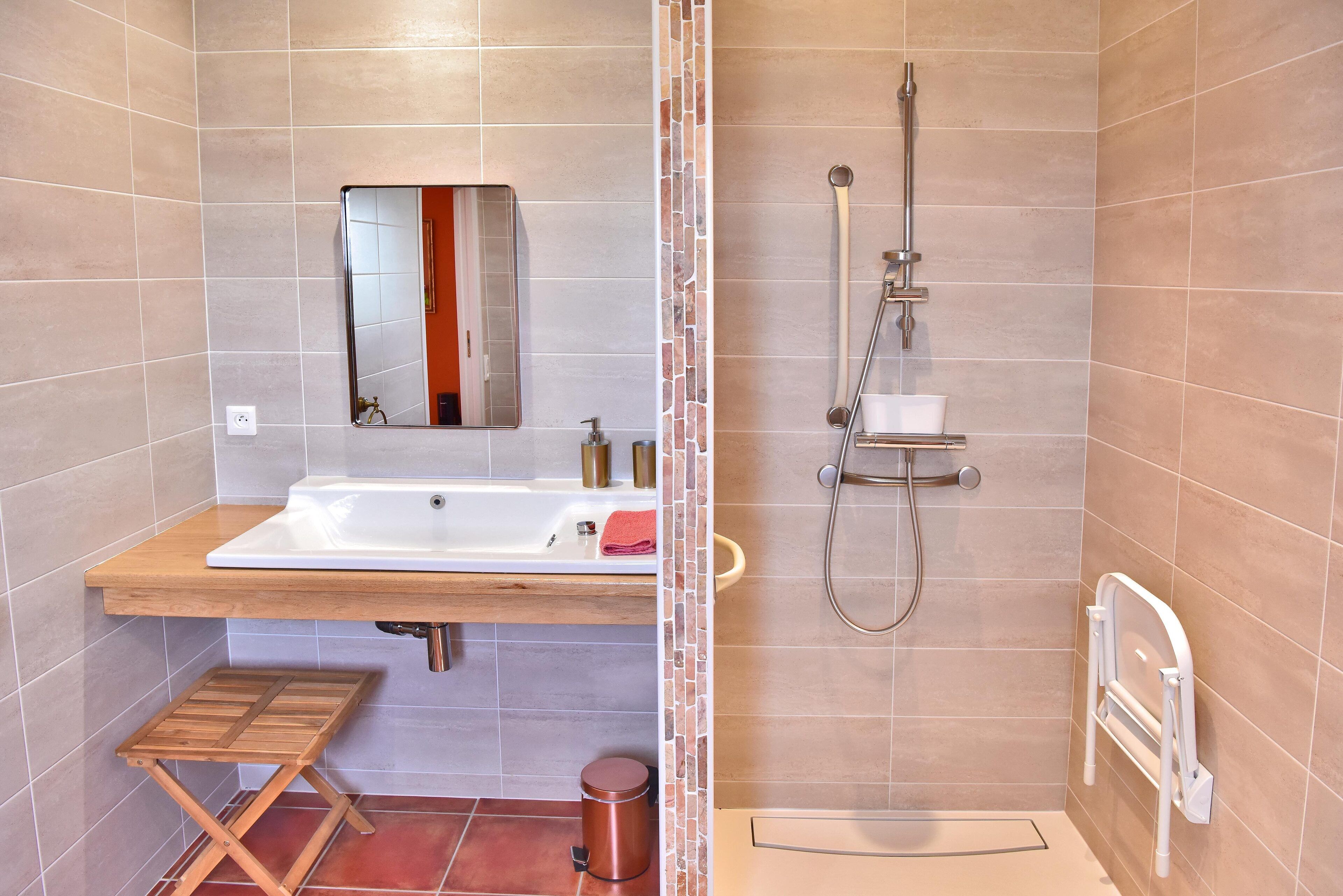 A bathroom with a wooden vanity, a mirror, a shower with a handheld showerhead, and a white toilet.
