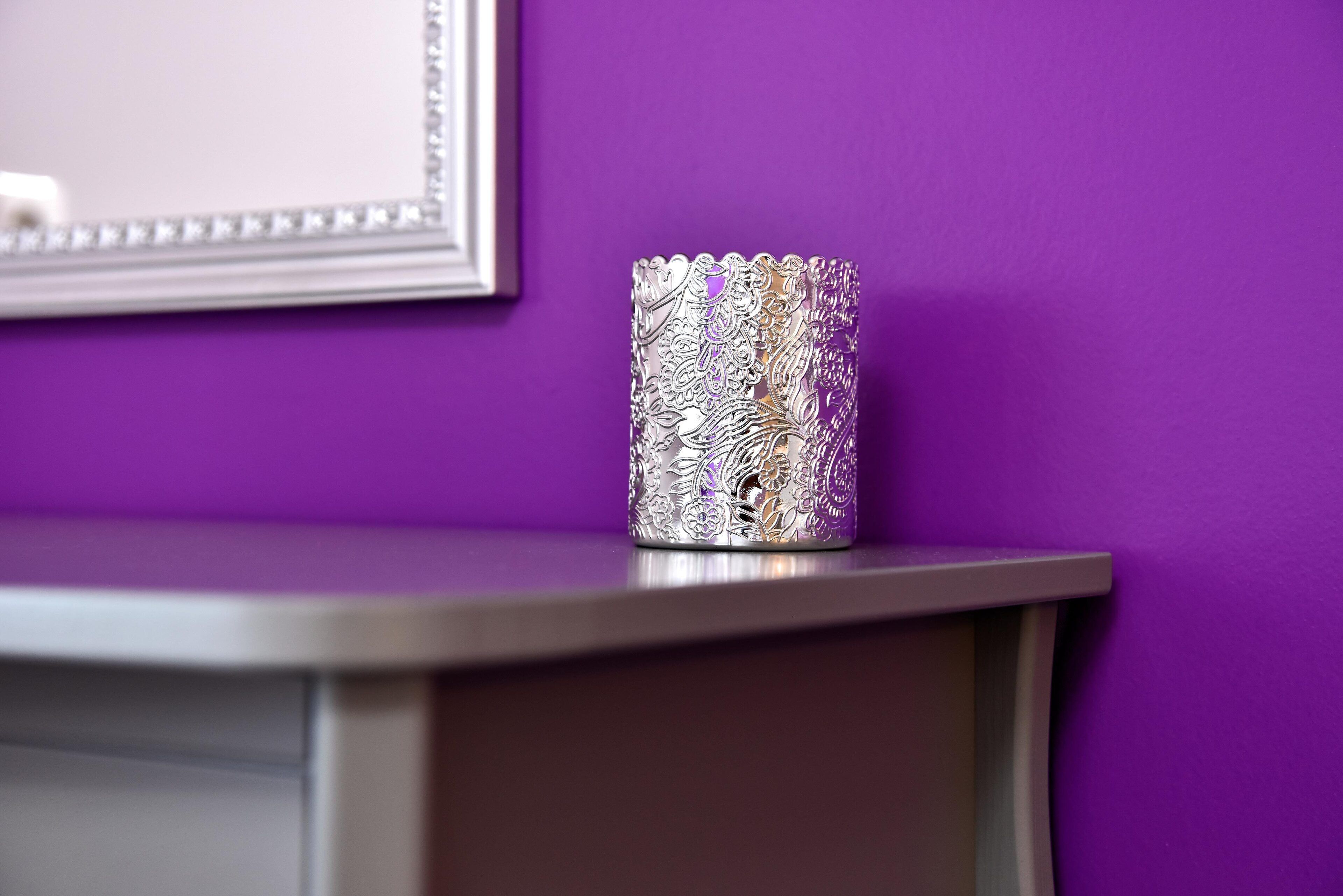 Un vase métallique au décor complexe, posé sur une surface incurvée devant un mur violet.