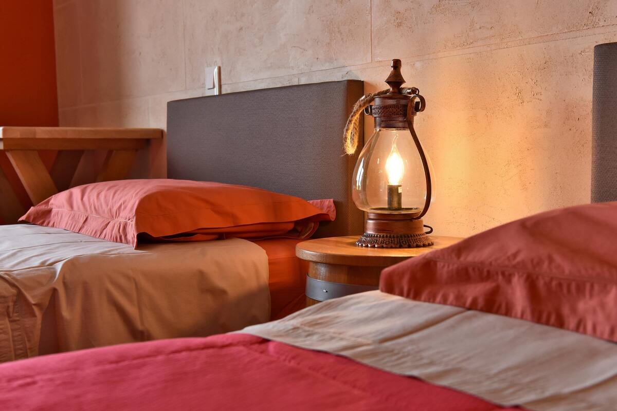 A bed with a wooden headboard, a bedside table with a lantern, and a red pillow.