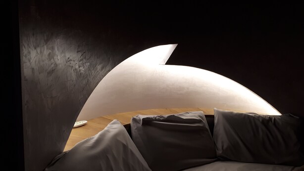 A bedroom with a curved ceiling, a wooden bedside table, and a bed with grey bedding. - Domaine d'Arcalis (Archiac)