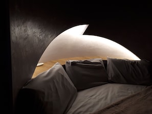 A bedroom with a curved ceiling, a wooden bedside table, and a bed with grey bedding. - Domaine d'Arcalis (Archiac)