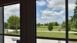 A view from a window with a table and chairs outside, a lawn, and trees. - Domaine d'Arcalis (Archiac)