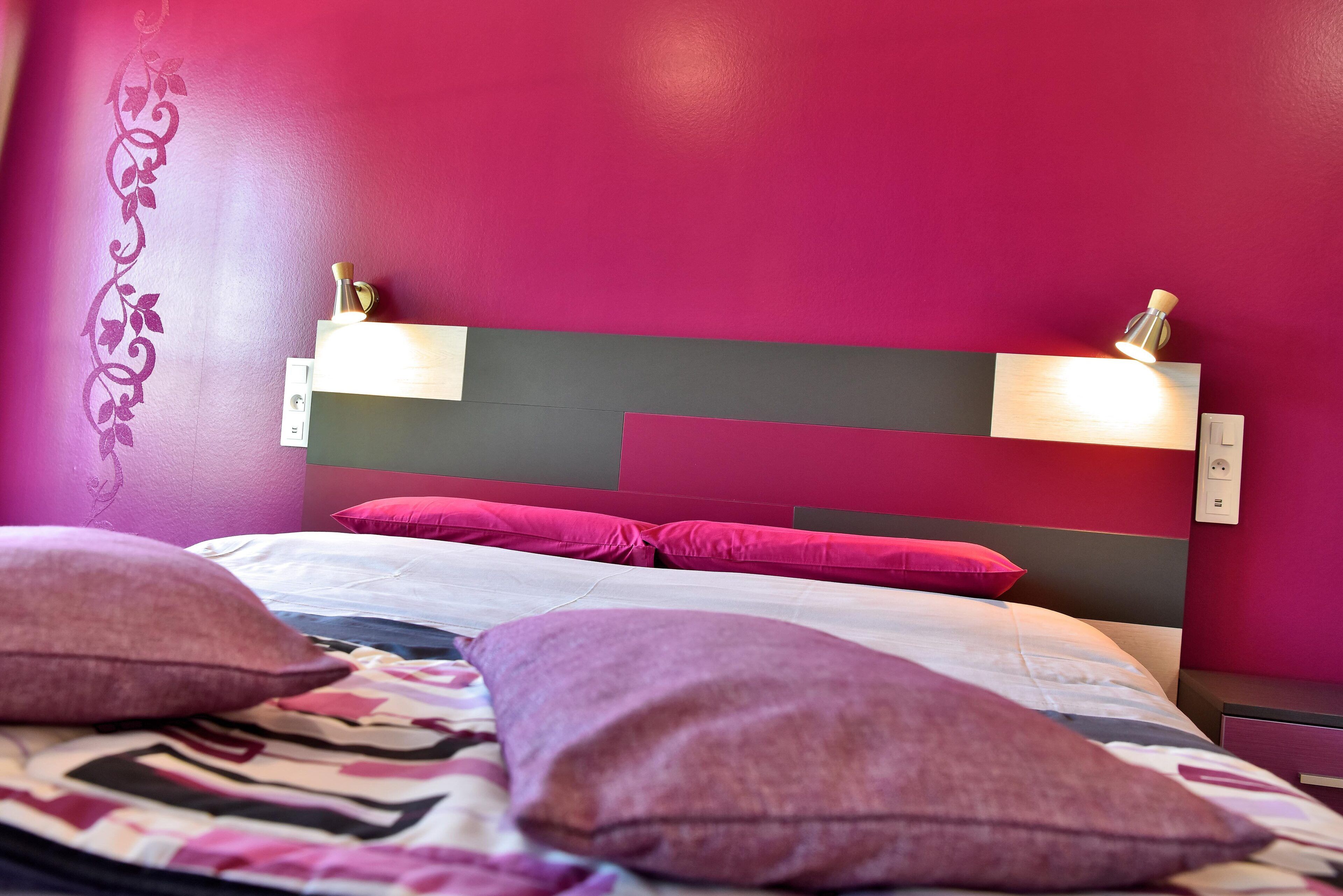 Una cama con cabecera, varios almohadones y una pared con diseño decorativo.