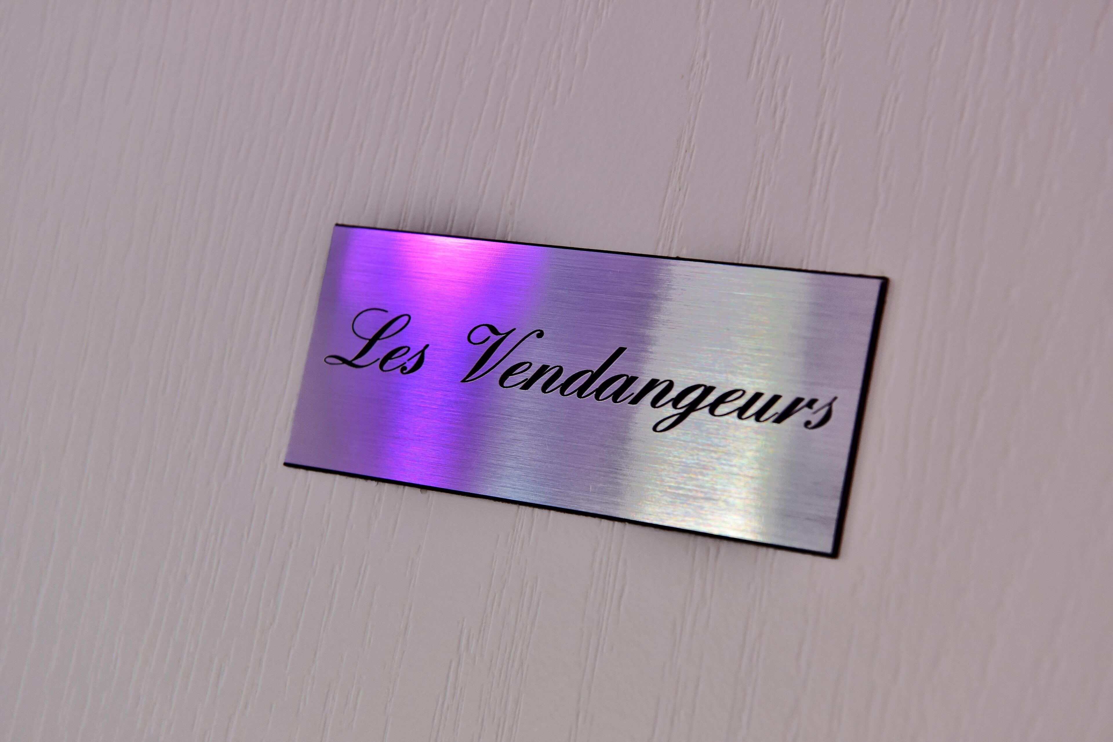 Una placa metálica con la inscripción 'Les Vendangeurs' en una pared de color claro.