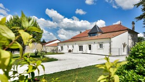 A white building with a red-tiled roof, a gravel driveway, and a well-maintained lawn. - Domaine d'Arcalis (Archiac)