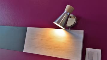 Un luminaire mural fixé au mur, doté d’un socle en bois et d’un abat-jour métallique, placé au-dessus d’un panneau en bois sur un mur violet.