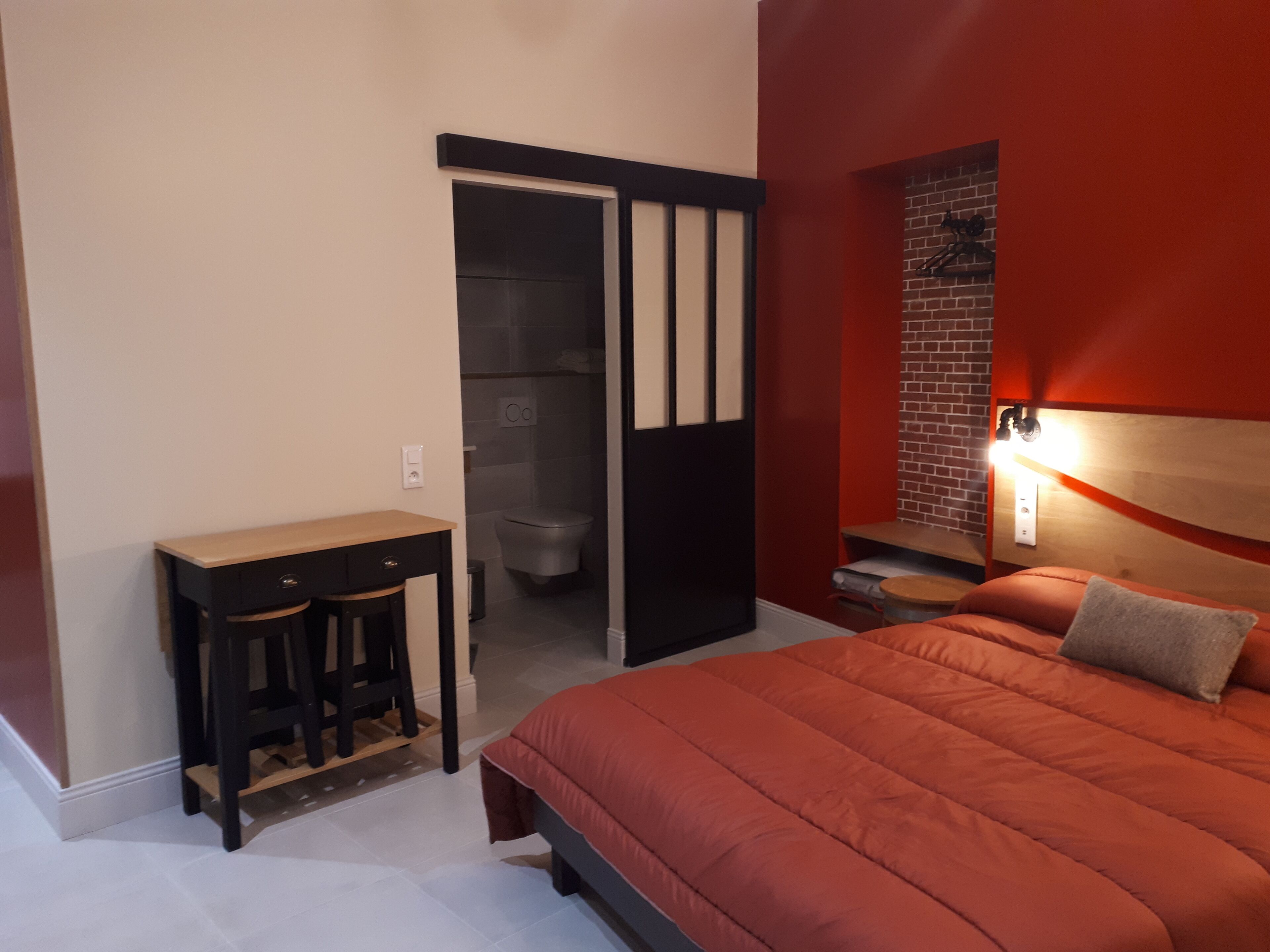 Ein Schlafzimmer mit Bett, Schreibtisch und einem durchgegangenen Tür sichtbar liegenden Badezimmer.