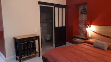 Ein Schlafzimmer mit Bett, Schreibtisch und einem durchgegangenen Tür sichtbar liegenden Badezimmer.