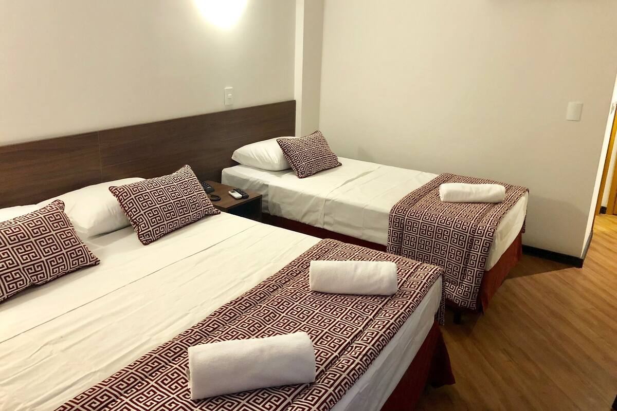 Ett hotellrum med två sängar, var och en med mönstrat sänglinne och kuddar, ett nattduksbord med en fjärrkontroll och en luftkonditioneringsenhet på väggen.