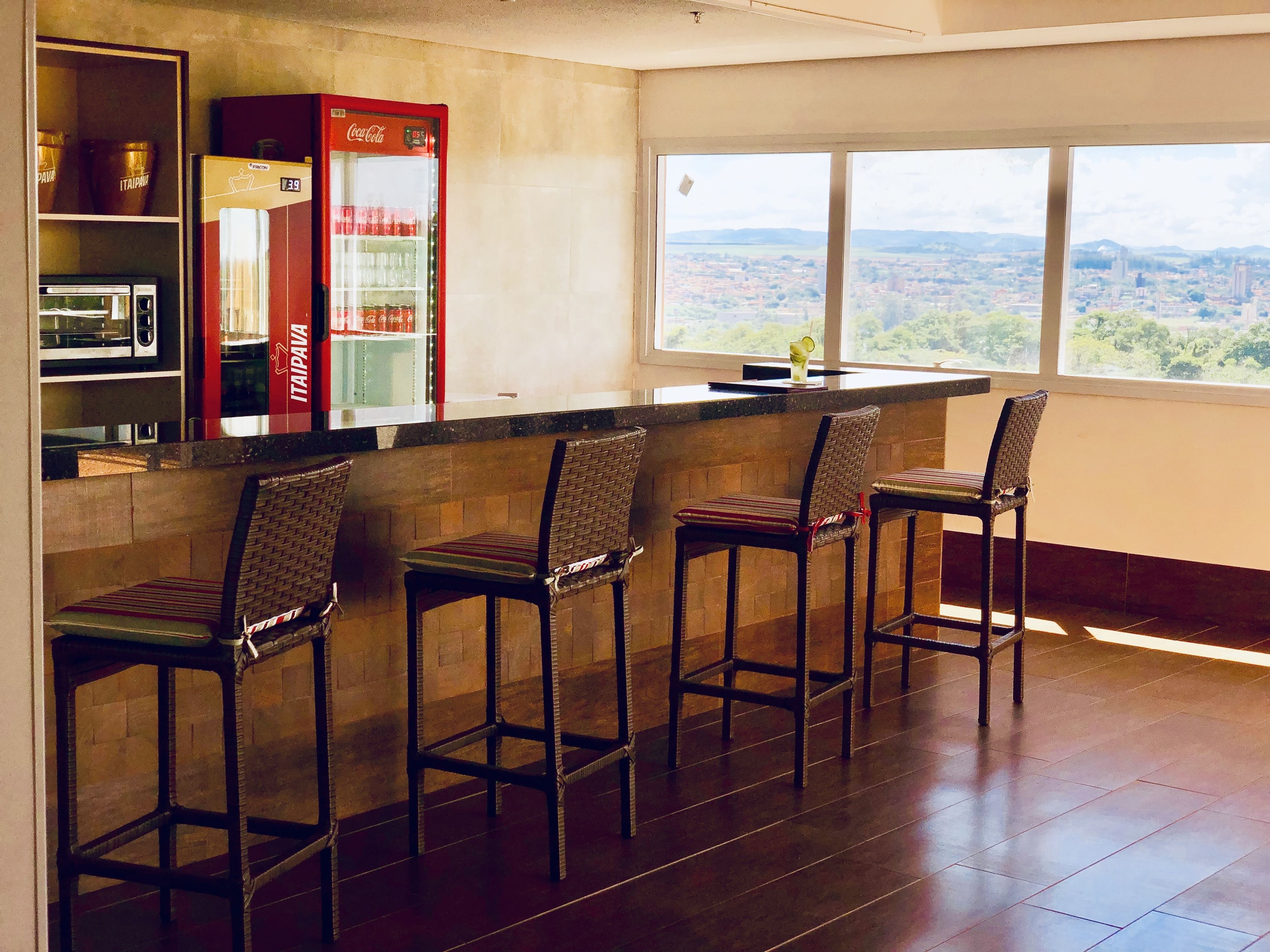Una cocina con barra, un refrigerador y un refrigerador Coca-Cola. Hay cuatro taburetes de bar y una ventana con vistas a la ciudad.