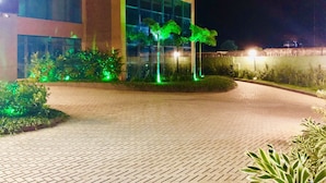 A modern building with a paved entrance area and green-lit trees.