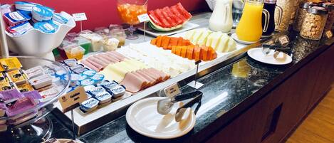 A buffet with various food items including meats, cheeses, fruits, and beverages.