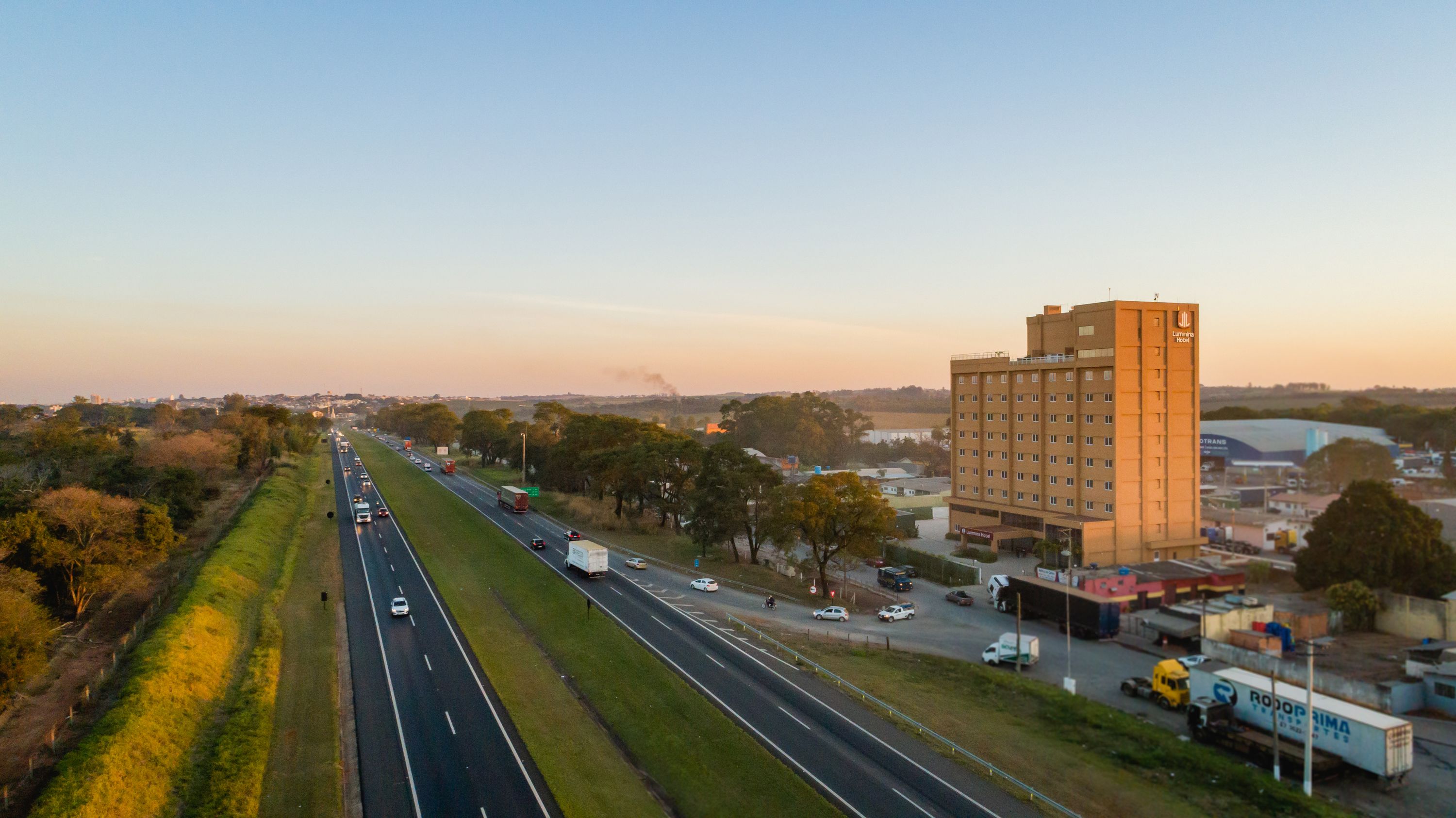 Une autoroute à plusieurs voies, avec de nombreux véhicules, un grand bâtiment d’hôtel portant une enseigne, et une végétation luxuriante tout autour.