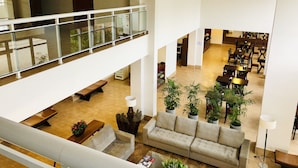 A spacious, multi-level hotel lobby with a high ceiling, a glass railing on the upper level, and a seating area with a sofa and coffee table.