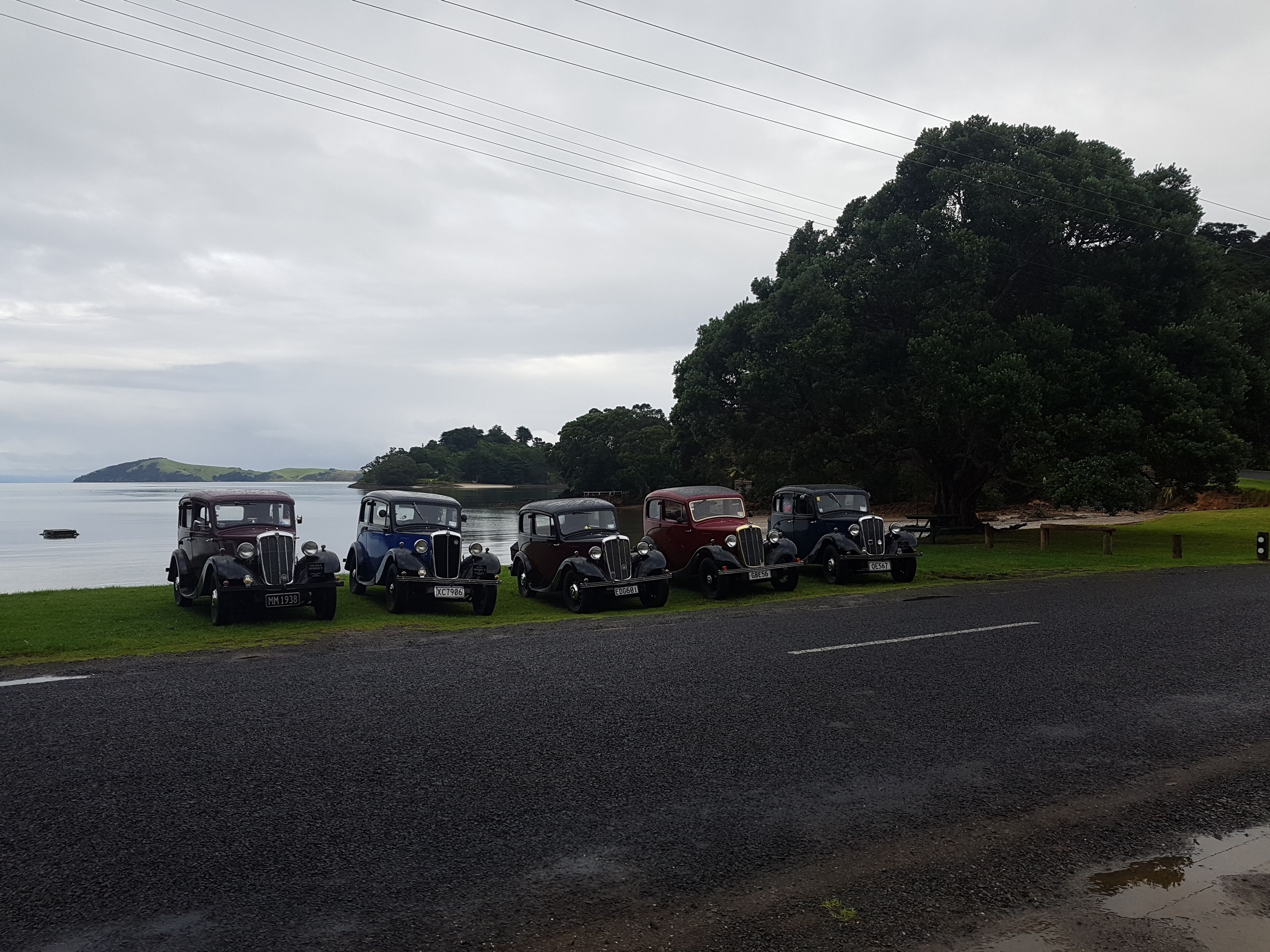 A row of vintage cars parked by a lakeside road.