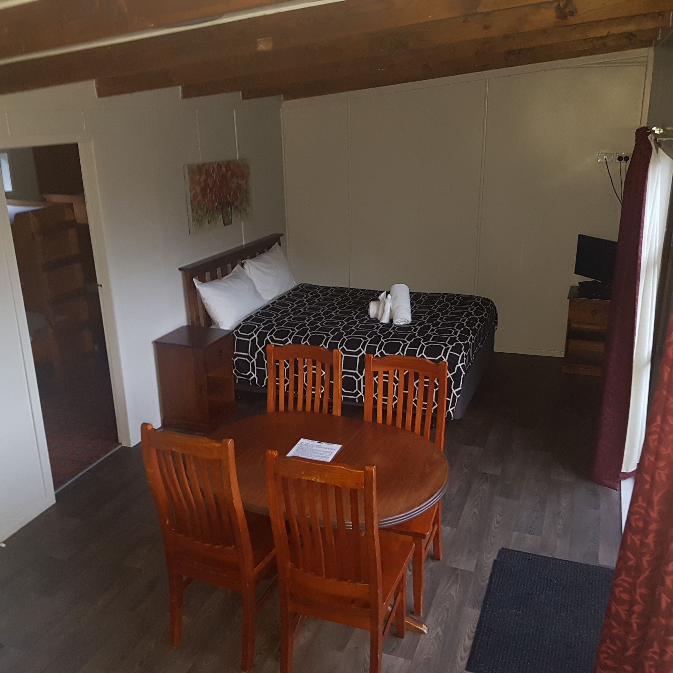 A small, cozy room with a bed, a wooden table with chairs, and a television.