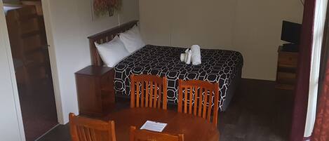 A small, cozy room with a bed, a wooden table with chairs, and a television.