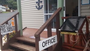 A wooden staircase leading to a building entrance with a sign reading "OFFICE" and another sign warning "WATCH OUT FREE RANGE CHILDREN". - Oamaru Bay Tourist Park (Coromandel)