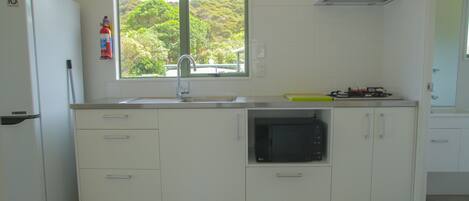 Una cocina con refrigerador blanco, microondas, lavamanos y ventana con vista a follaje.