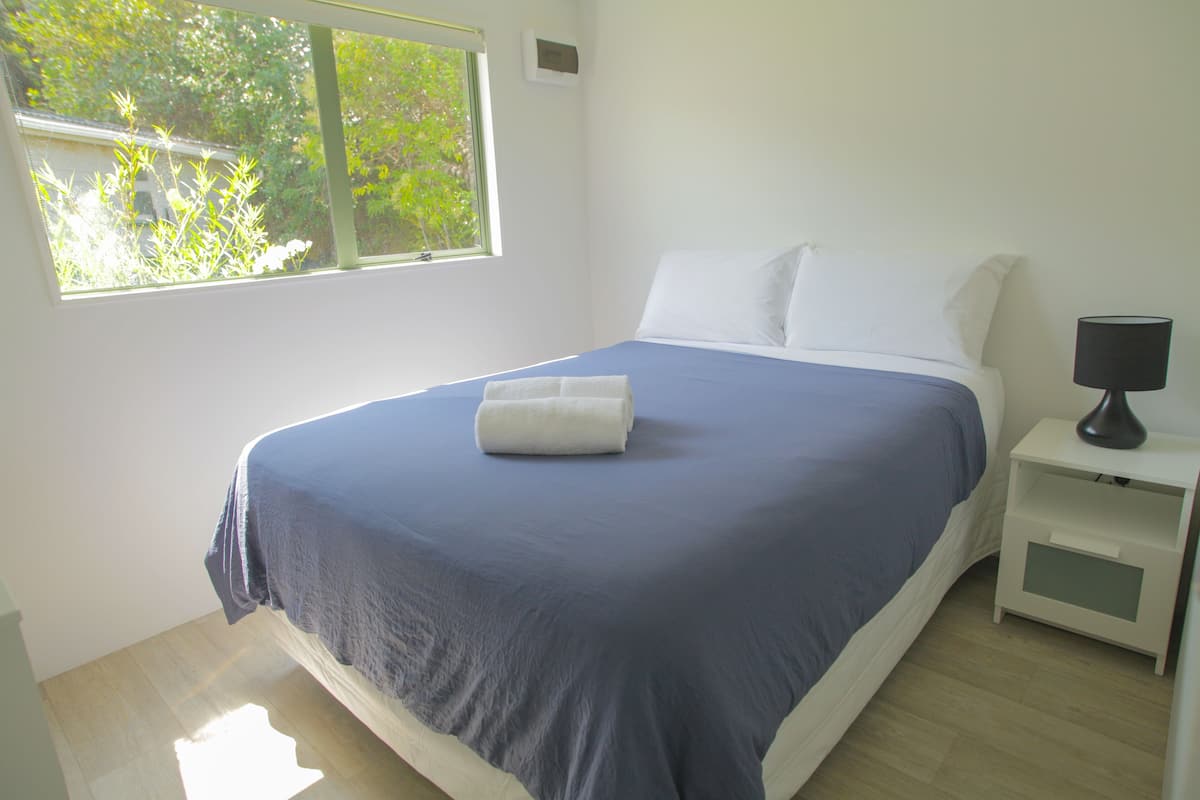 A neatly made bed with a blue and white bedspread, a white pillow, and a white bedside table with a lamp.