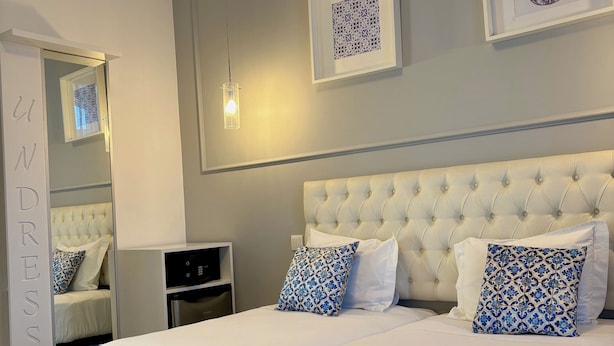 A neatly arranged bedroom with a large bed, a bedside table, a wardrobe, and two framed artworks on the wall. - Lisbon City Inn Hotel by City Hotels (Lisbon)