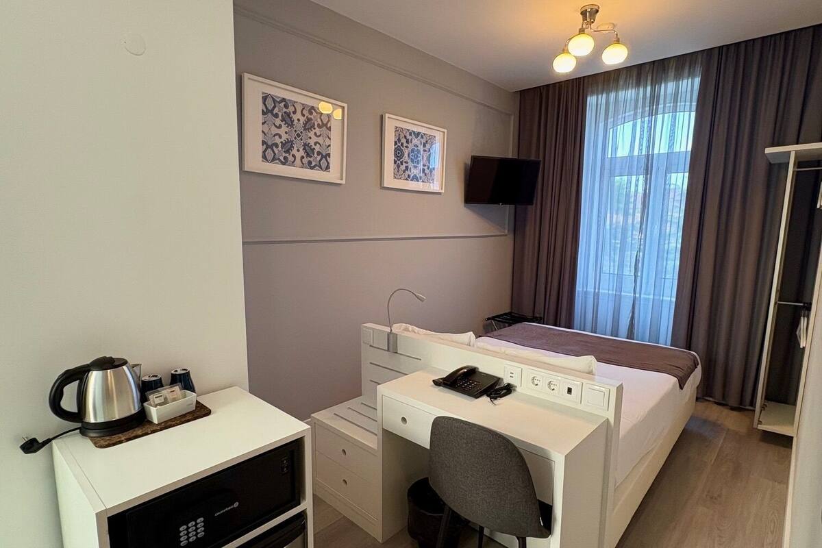 Una camera d'albergo compatta con un letto, una scrivania, angolo cottura e televisione.