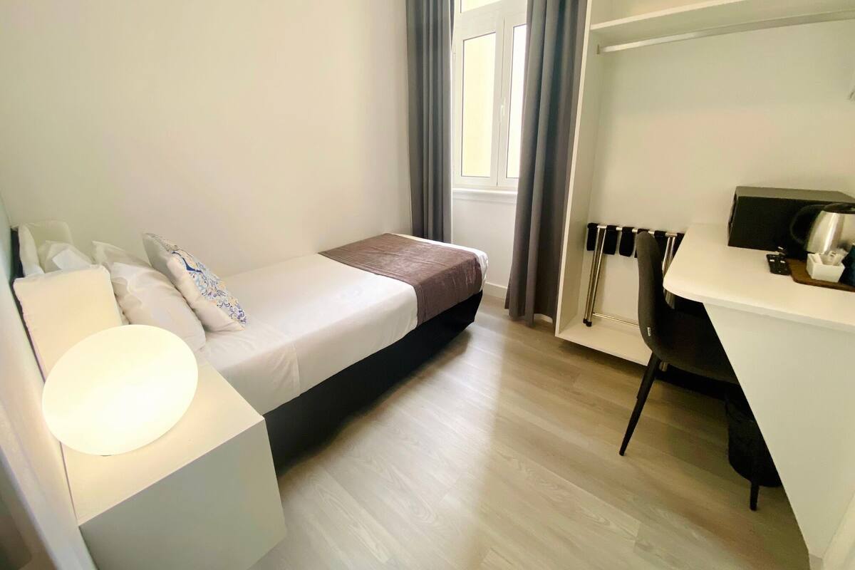 Una camera da letto piccola e moderna con un letto singolo, una scrivania e una sedia.