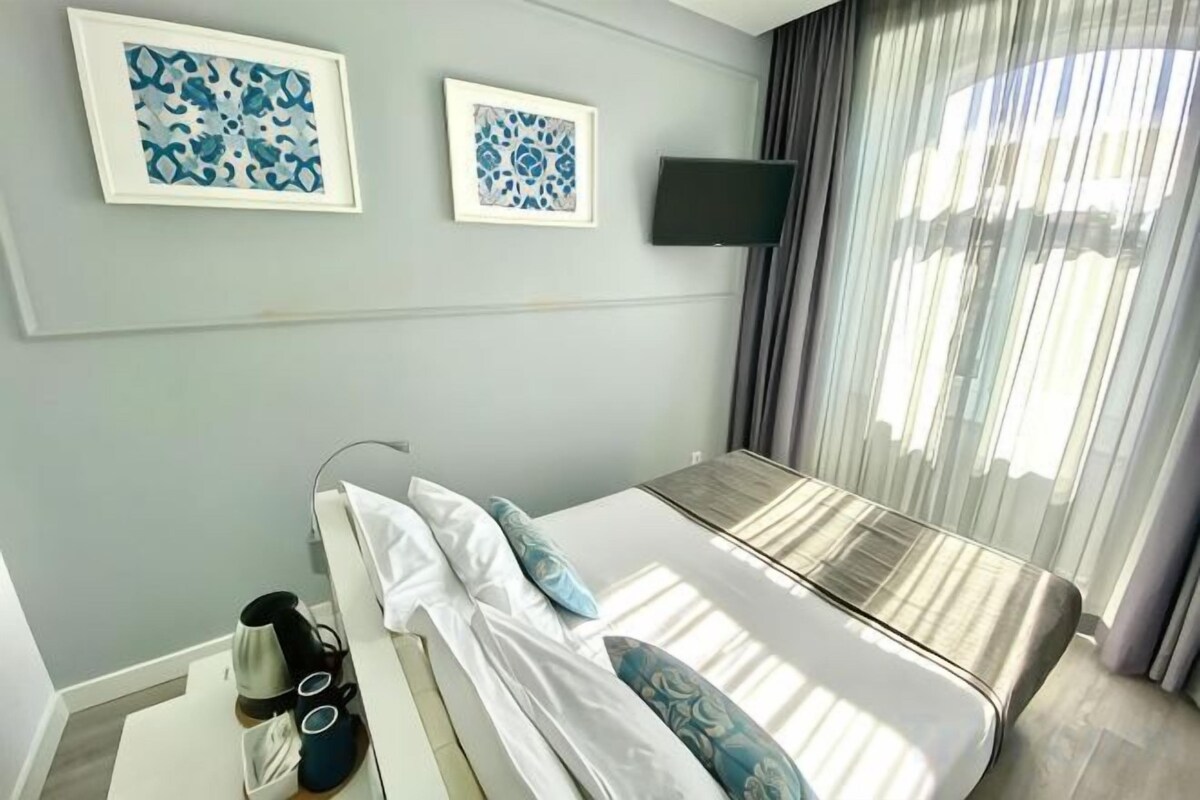 A hotel room with a bed, a flat-screen TV mounted on the wall, and a window with curtains.