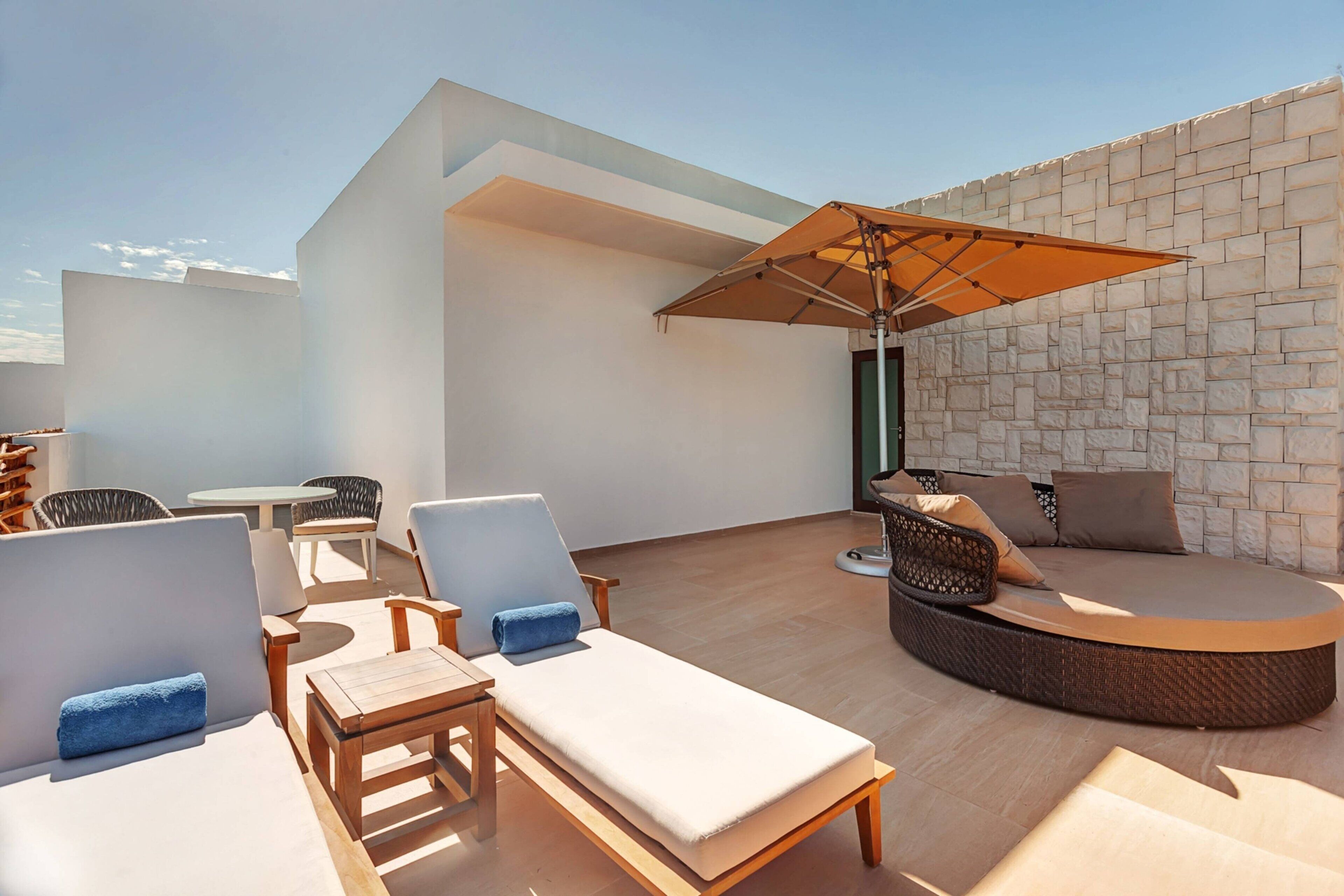 Um lounge no terraço com parede de pedra, cadeiras de descanso, uma área de estar circular e uma mesa.