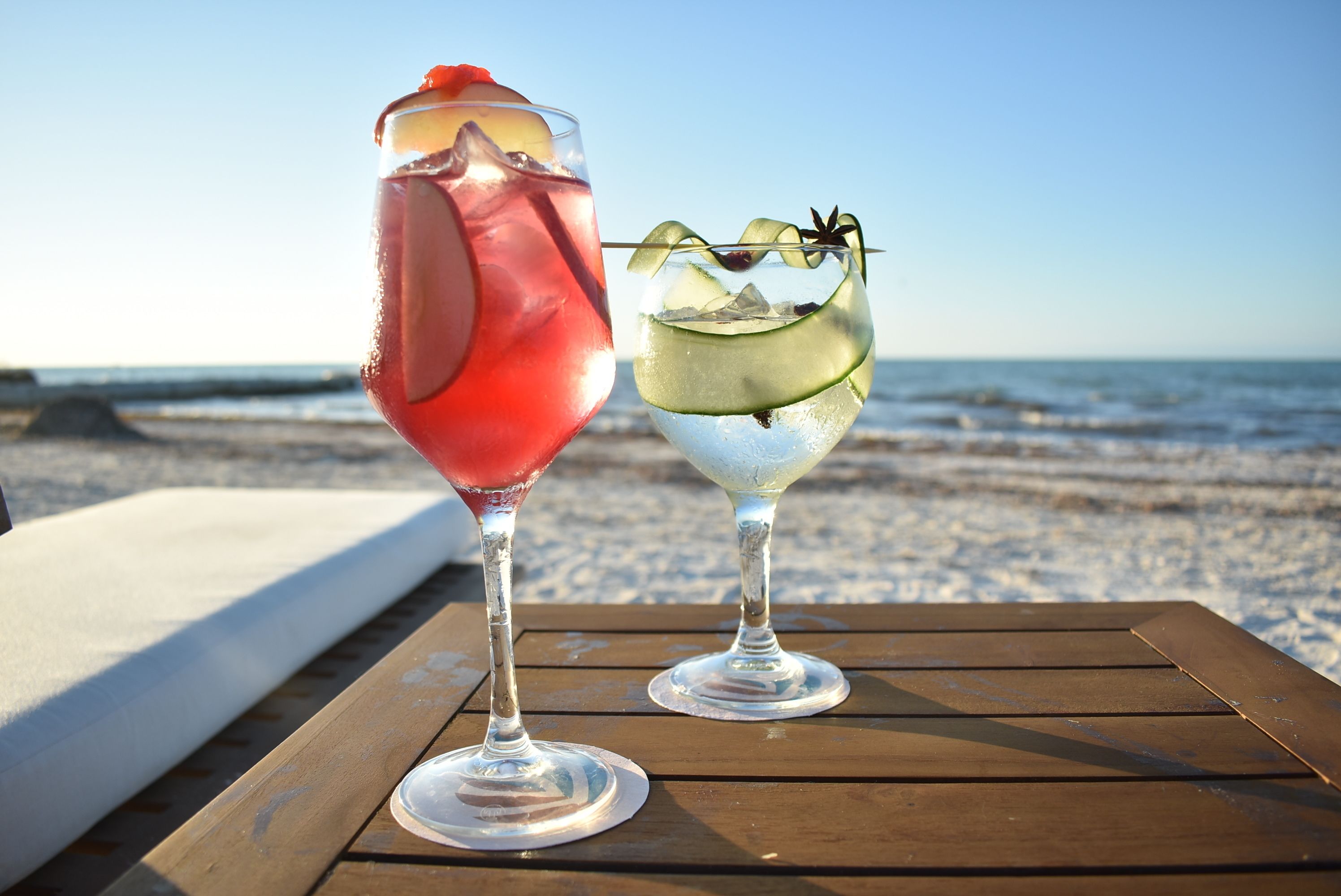 Dos bebidas sobre una mesa de madera, con una playa y el océano al fondo.