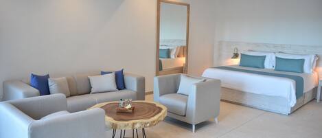 A modern hotel room with a large bed, two sofas, a round coffee table, and a large mirror.
