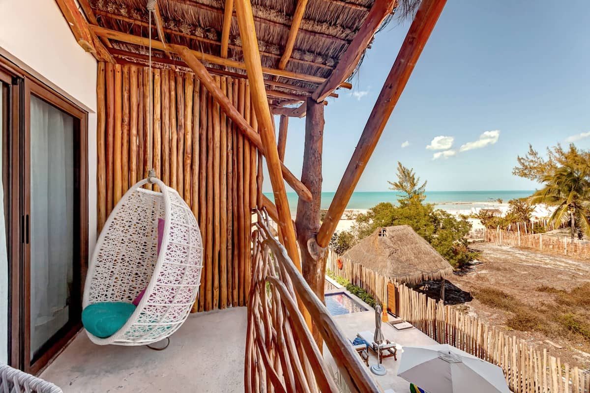 Uma varanda com uma cadeira suspensa, piscina e vista para a praia.