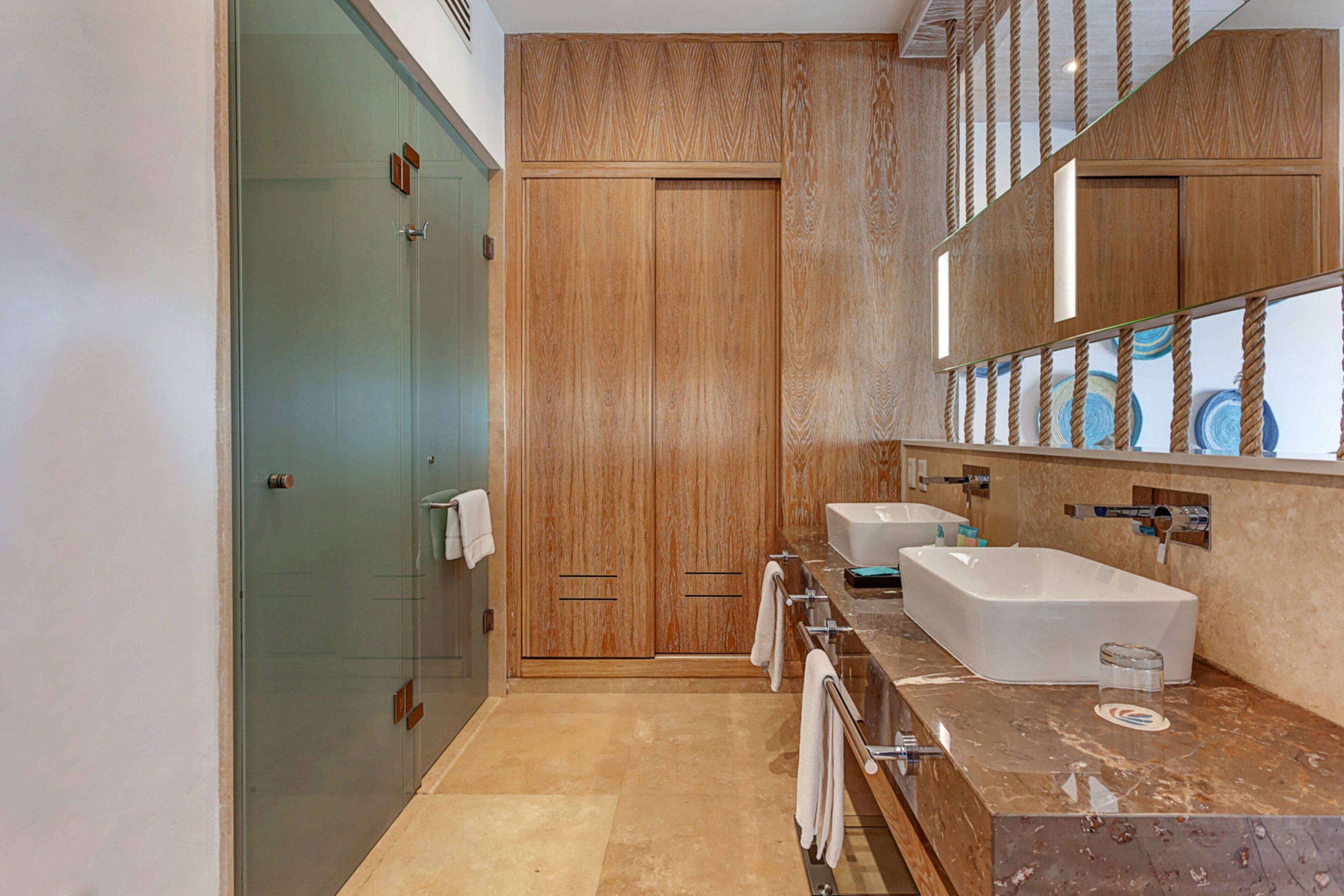 A modern bathroom with a glass shower enclosure, wooden vanity cabinets, a large mirror, and a marble countertop.