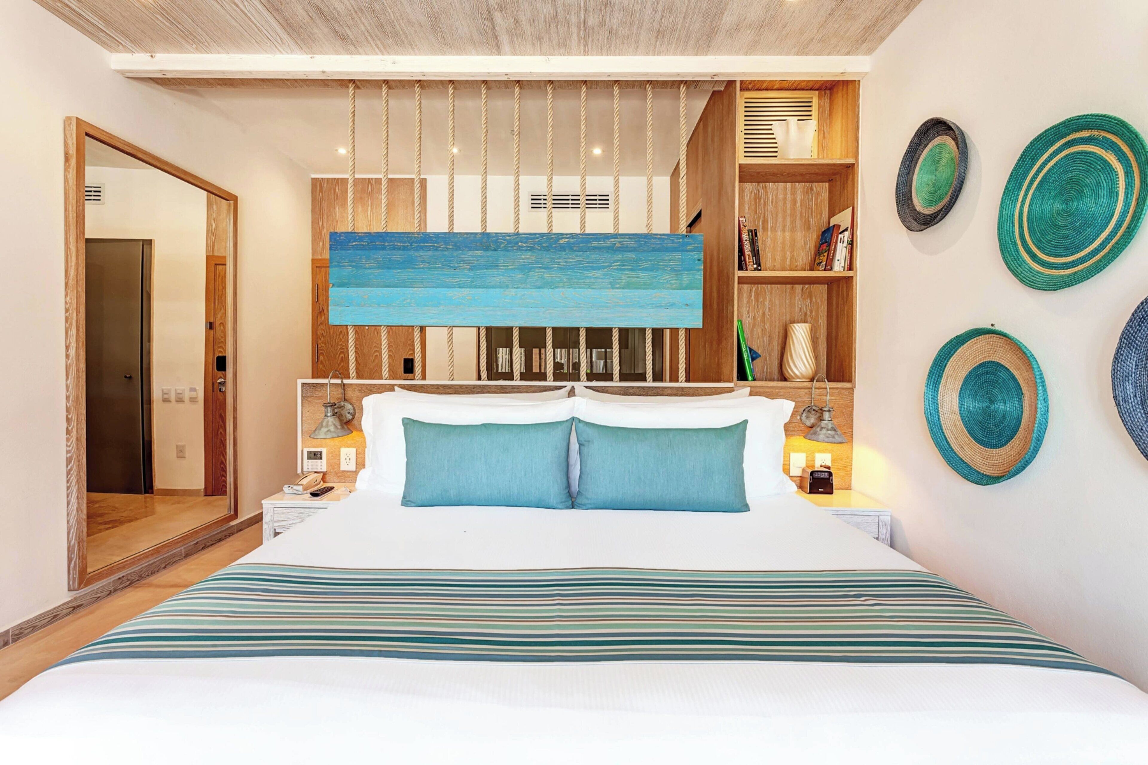 Een hotelkamer met een groot bed, een houten hoofdeinde, uitzicht op de gang en een plankje met decoratieve spullen.