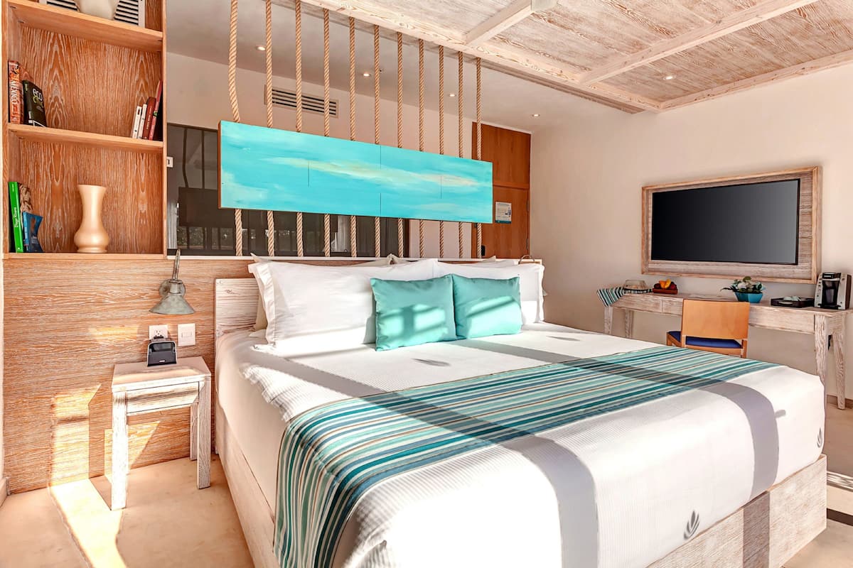 Quarto de hotel moderno com uma cama grande, uma escrivaninha, uma televisão e uma estante de livros.