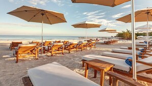 A beachside lounge area with wooden lounge chairs and tables, beige umbrellas, and a view of the ocean. - Mystique Holbox by Royalton, A Tribute Portfolio Resort (Isla Holbox)