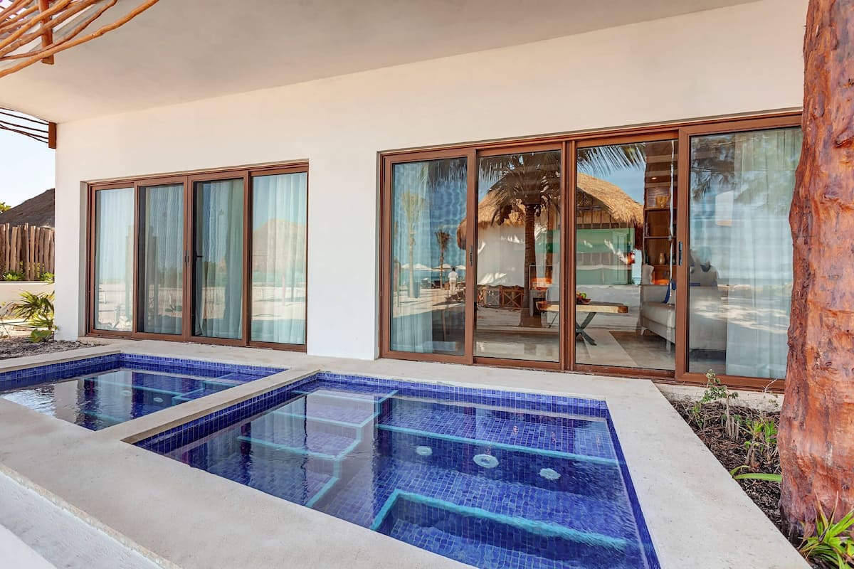 Uma casa moderna com piscina, amplas portas de vidro deslizantes e um telhado de palha visível pelas janelas.