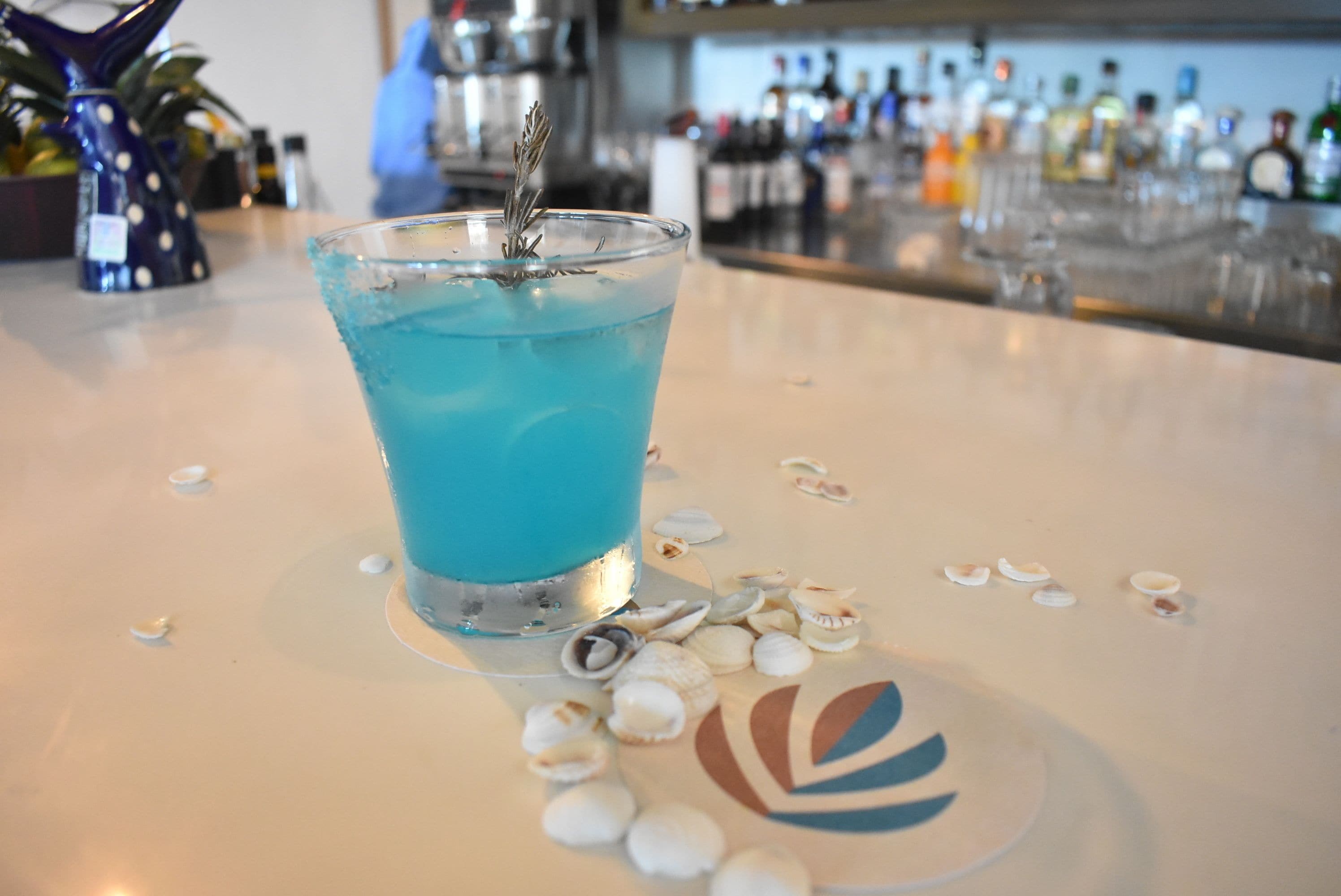 Un espace bar avec une boisson bleue, des coquillages disposés çà et là et un logo décoratif sur le comptoir.