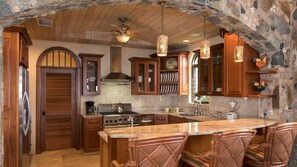 A kitchen with wooden cabinets, a central island, and a stone archway. - Rhapsody: Luxury! Sunset Views! Full AC! Pool! (St. John)