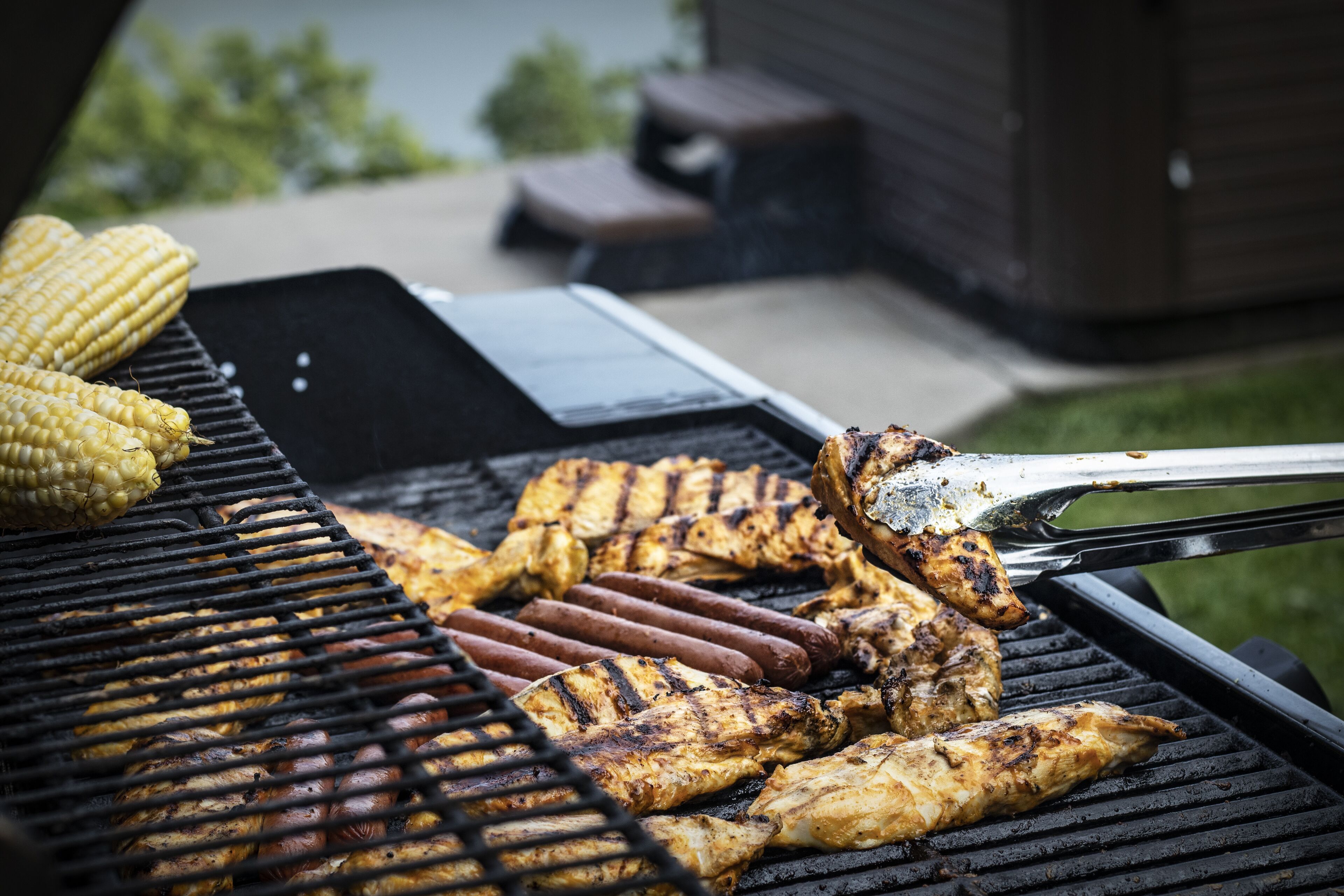 A grill with various meats and corn being cooked outdoors.