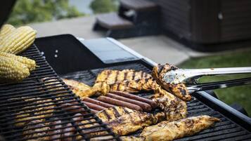 A grill with various meats and corn being cooked outdoors.